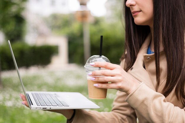 ドリンクを飲みながら屋外のラップトップに取り組んでいる女性