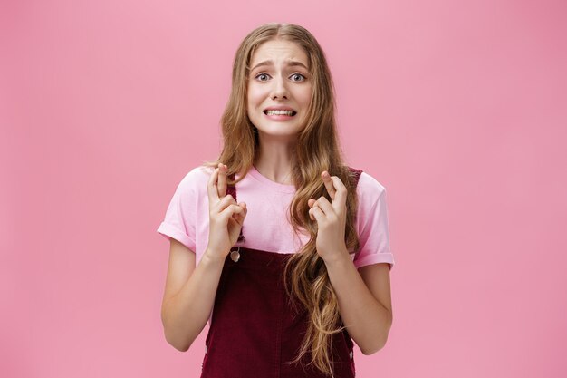 Woman overreacting feeling worried for important result waiting nervously crossing fingers for good luck clenching teeth and frowning looking concerned at camera, praying hopefully for wish come true.