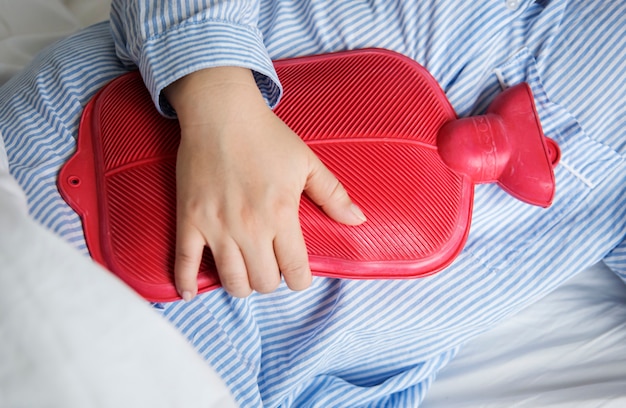 Free photo a woman in pain holding a hot water bottle