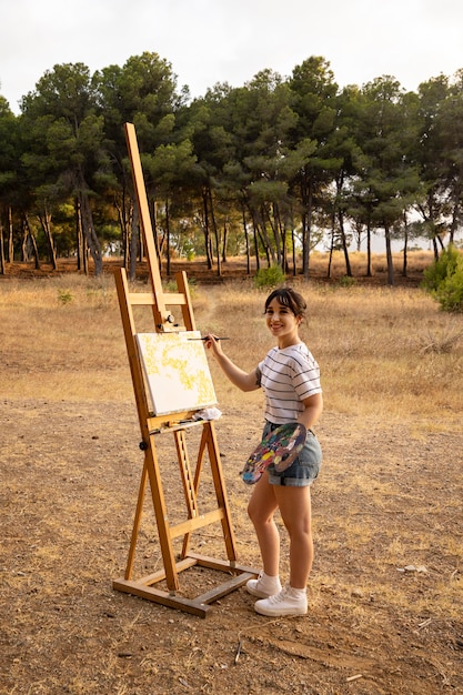 Foto gratuita donna dipinto su tela all'aperto nella natura