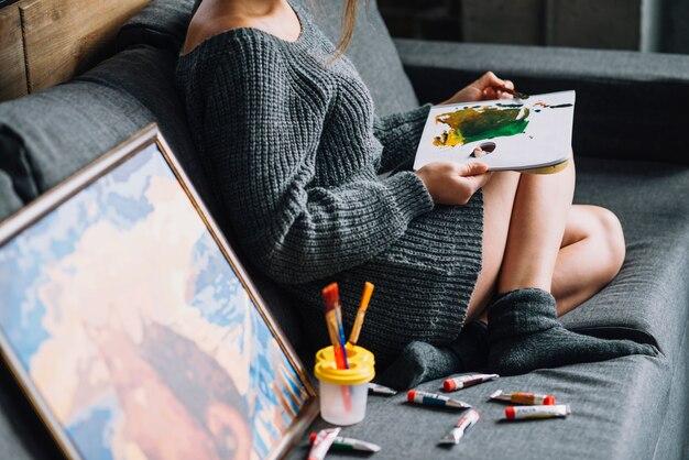 Woman painting on couch next to painting