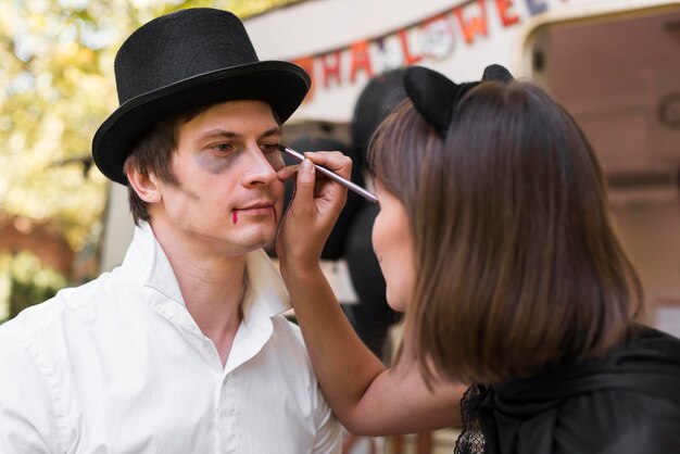 Woman painting man's face outdoors