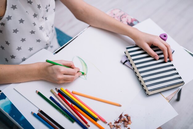 鉛筆とノートのセットを持つテーブルで紙に絵を描く女