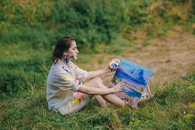 Woman painting a picture sitting on the grass