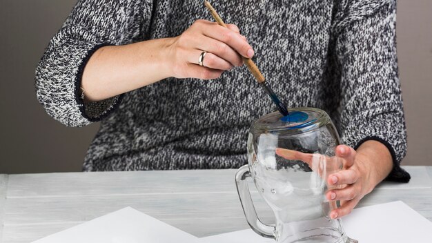 Woman painting on transparent glass jar with paint brush