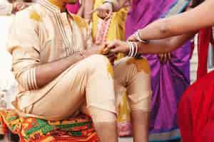 Free photo woman paints indian groom's knees and face with turmeric paste