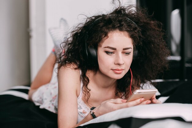 Woman in pajamas lies on bed listening to the music