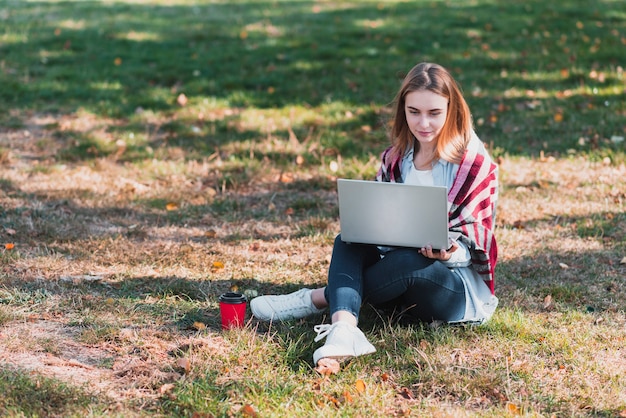 Женщина в парке работает на ноутбуке