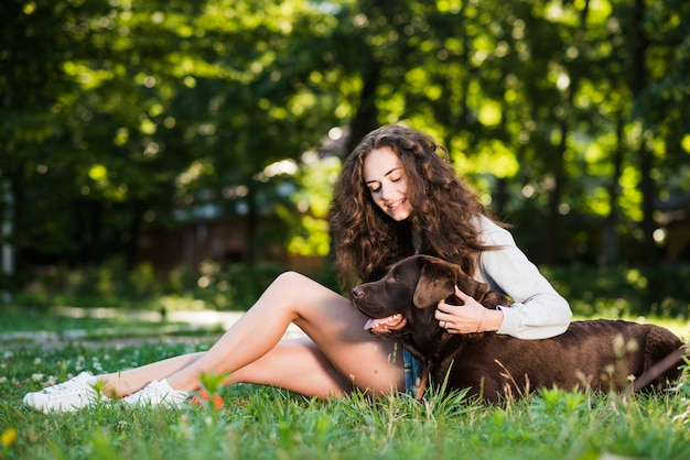 Woman patting her dog sitting on grass in park