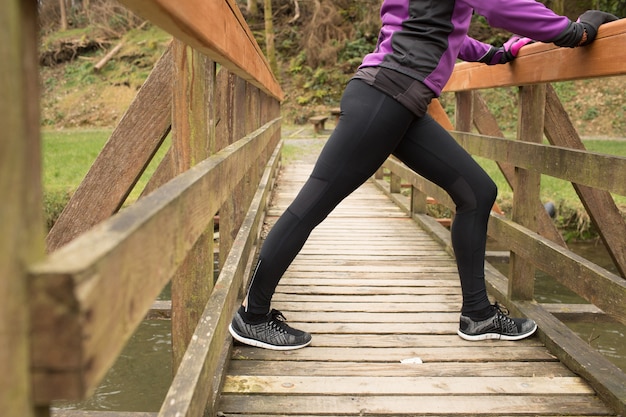 Foto gratuita donna che esegue esercizio di stretching sul ponte nella foresta