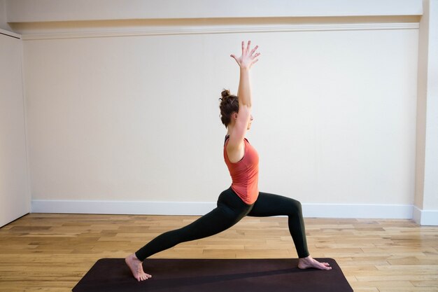 Woman performing warrior pose on exercise mat