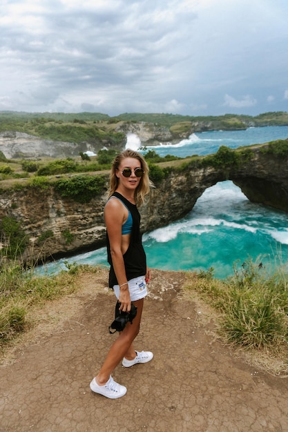 Женщина-фотограф-путешественница, фотографирующая достопримечательности на камеру, пляж Ангела Биллабонг, остров Нуса-Пенида, Бали, Индонезия.