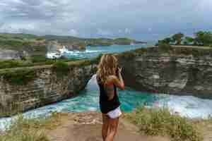 Free photo woman photographer traveler photographing landmarks on camera,  angel's billabong beach, nusa penida island, bali, indonesia.