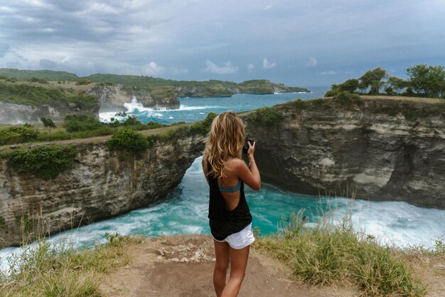 인도네시아 발리 누사 페니다 섬(Nusa Penida Island)의 엔젤 빌라봉(Angel's Billabong) 해변에서 랜드마크를 촬영하는 여성 사진작가입니다.