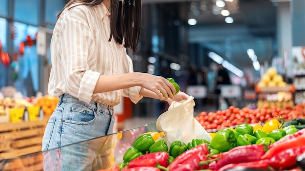 Free photo woman picking bell peppers in a reusable bag ecology earth day thematics