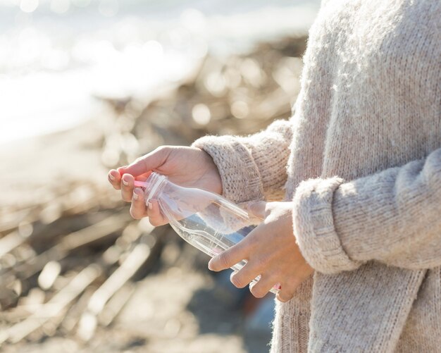 woman picking plastic bottle from sand