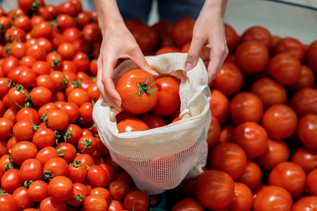 再利用可能なバッグでトマトを摘む女性 エコロジー アースデイのテーマ