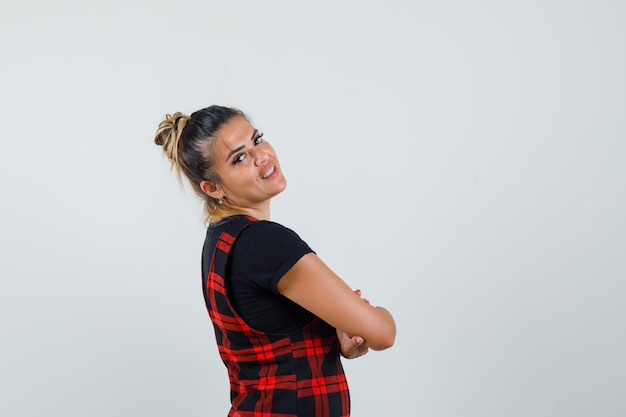 Woman in pinafore dress standing with crossed arms and looking confident .