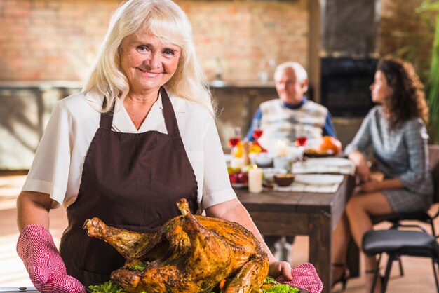 Woman in pinafore holding plate with baked ham