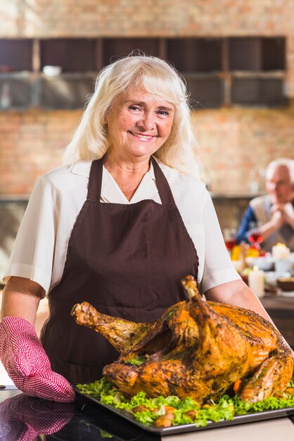 Woman in pinafore holding plate with roasted ham