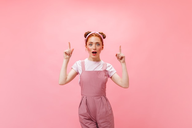 woman in pink jumpsuit got idea. Portrait of young redhead woman on pink background.