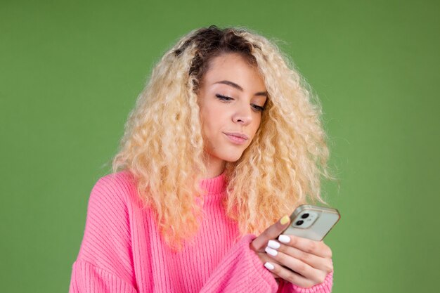 Woman in pink sweater on green holding mobile phone thoughtful