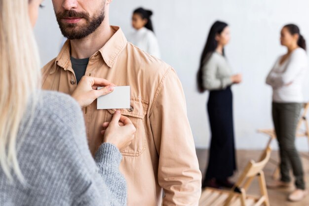 Woman pinning name tag on man's shirt at a group therapy session