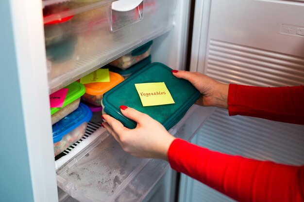 Женщина помещает контейнер с замороженной овощной смесью в морозильную камеру.