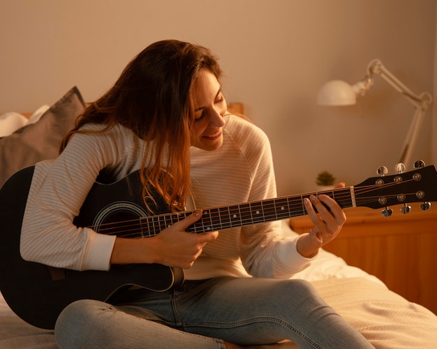 Woman playing guitar at home in bed