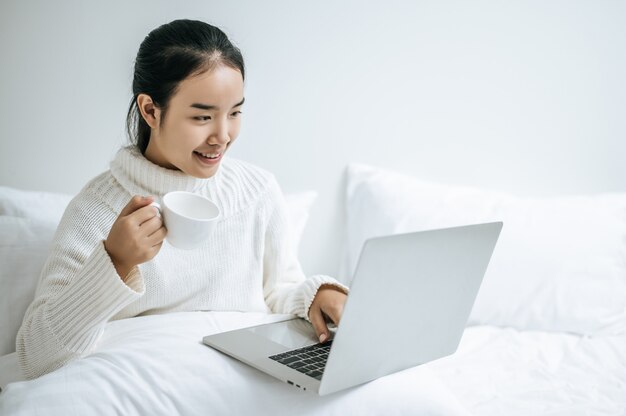 A woman playing a laptop and holding a coffee cup.