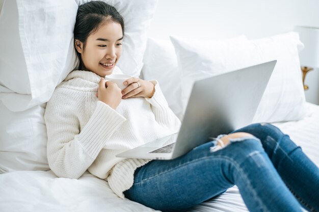 A woman playing a laptop and holding a coffee cup.