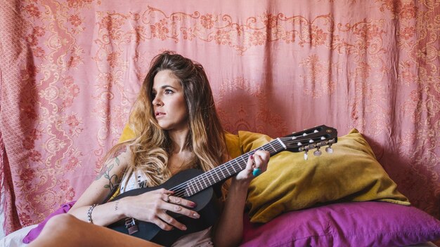 Woman playing ukulele near pillows