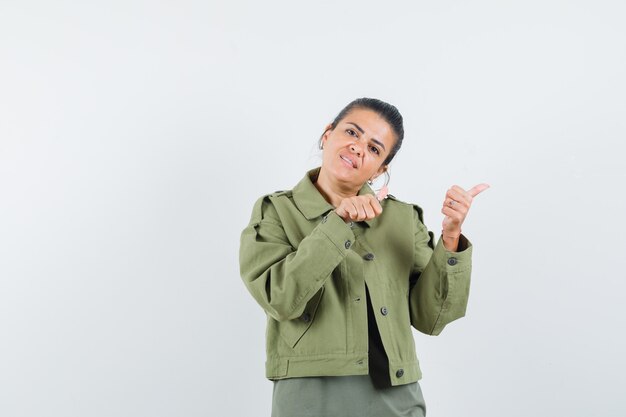 woman pointing aside with thumbs in jacket, t-shirt and looking jolly