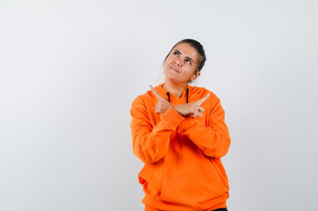 woman pointing away in orange hoodie and looking dreamy