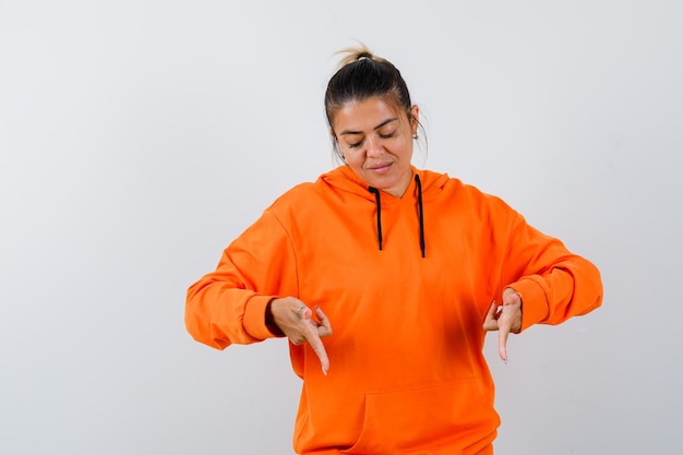 Woman pointing down in orange hoodie and looking focused