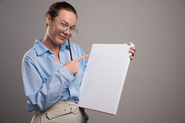 Woman pointing at empty canvas and brush on gray background