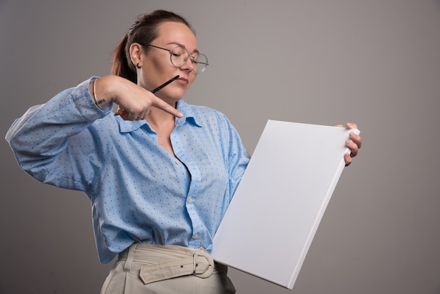 Free photo woman pointing at empty canvas and brush on gray background