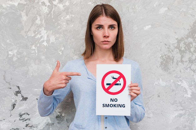 Бесплатное фото Женщина указывая пальцем на плакат для некурящих, стоя возле выветривания стены