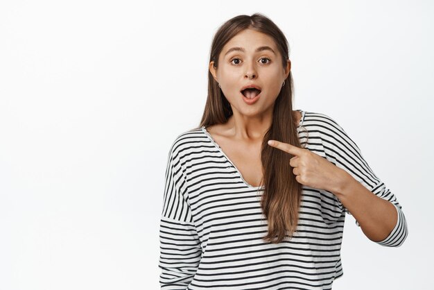 Woman pointing at herself with surprised face standing in casual clothes over white background