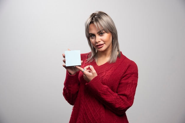 Woman pointing at memo pad on gray background.