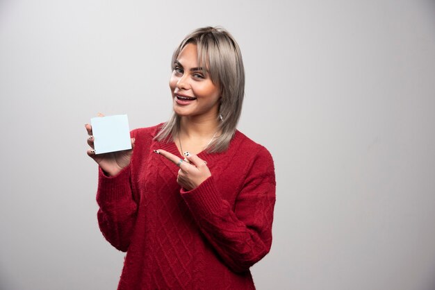 Woman pointing at memo pad on gray background.