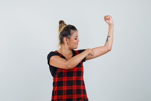 Free photo woman pointing at muscles of arm in pinafore dress and looking proud , front view.