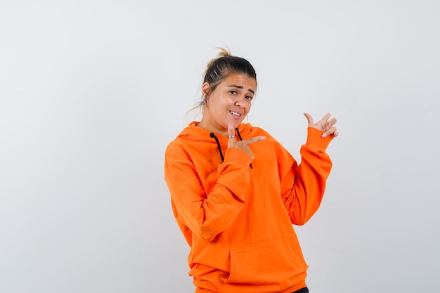 woman pointing to the right side in orange hoodie and looking confident