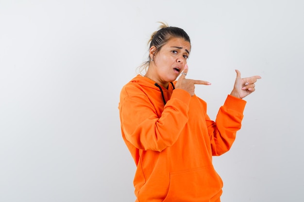 woman pointing to the right side in orange hoodie and looking confused