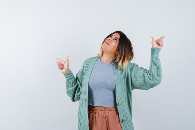 Woman pointing up in casual clothes and looking astonished , front view.