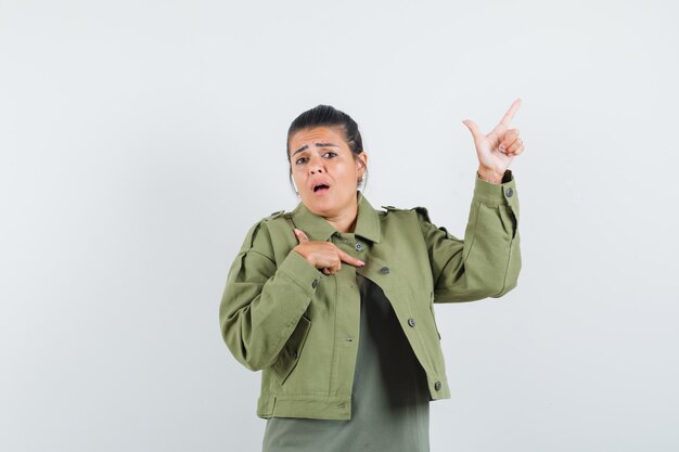 Woman pointing up in jacket, t-shirt and looking anxious