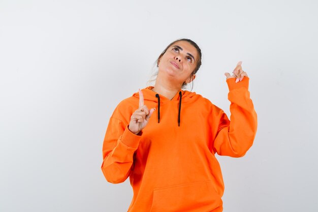 Woman pointing up in orange hoodie and looking dreamy