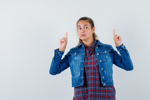 Woman pointing up in shirt, jacket and looking curious. front view.