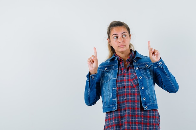 Woman pointing up in shirt, jacket and looking focused , front view.