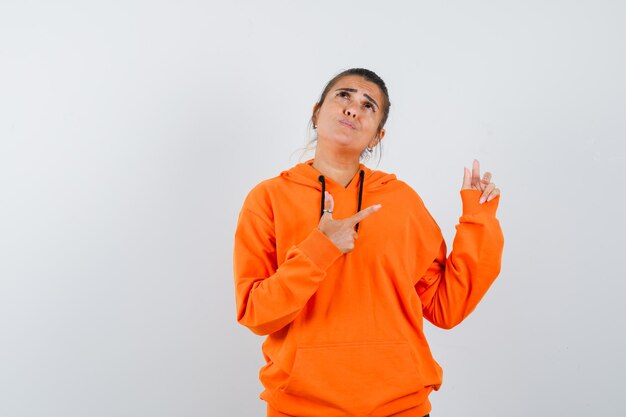 Woman pointing at upper right corner in orange hoodie and looking indecisive